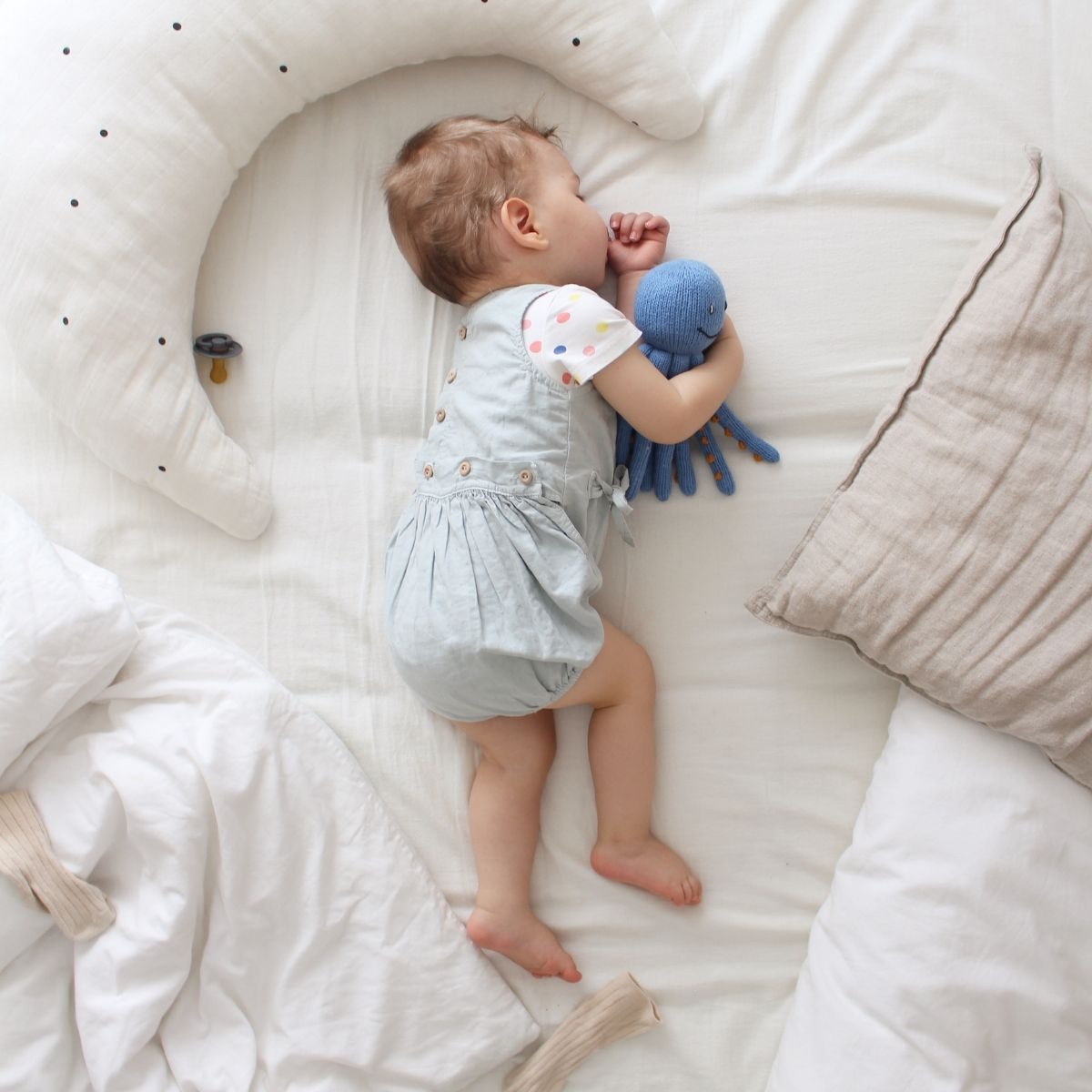 Baby kuschelt im Bett mit einem weichen Oktopus Kuscheltier aus Bio-Baumwolle und hält die Tentakel fest.