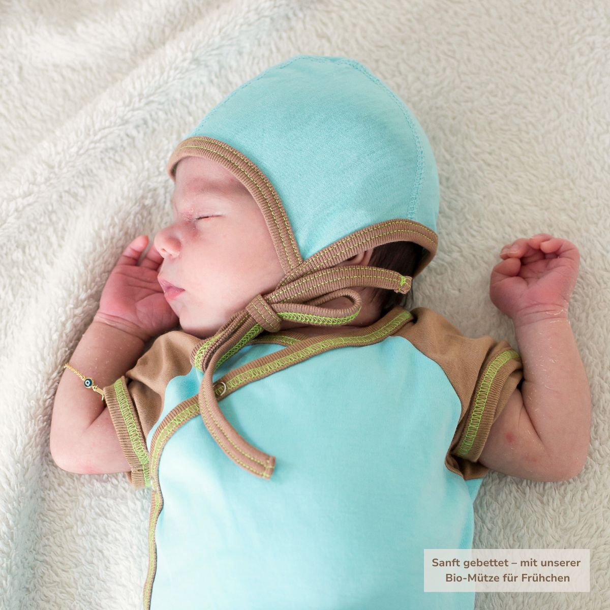 Frühchen mit hellblauer Bio-Mütze aus Pima Baumwolle, schlafend auf weichem Untergrund