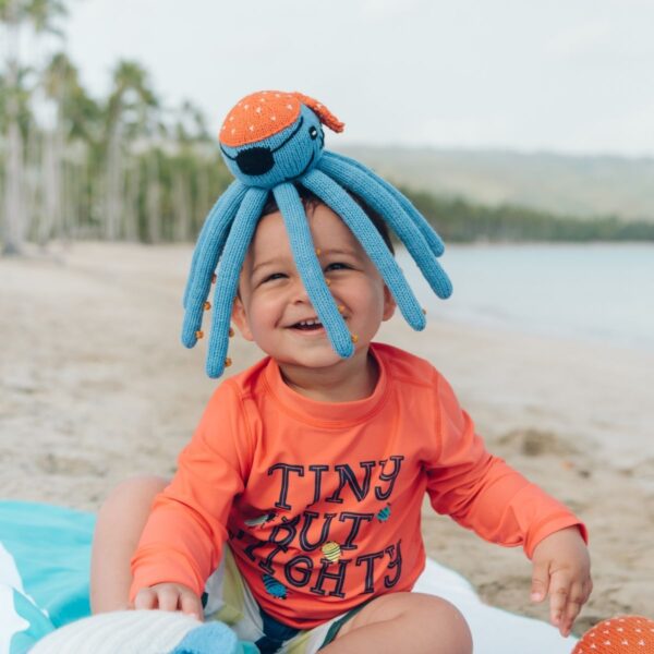 Lachendes Baby mit Kuscheltier Krake aus Bio-Baumwolle am Strand