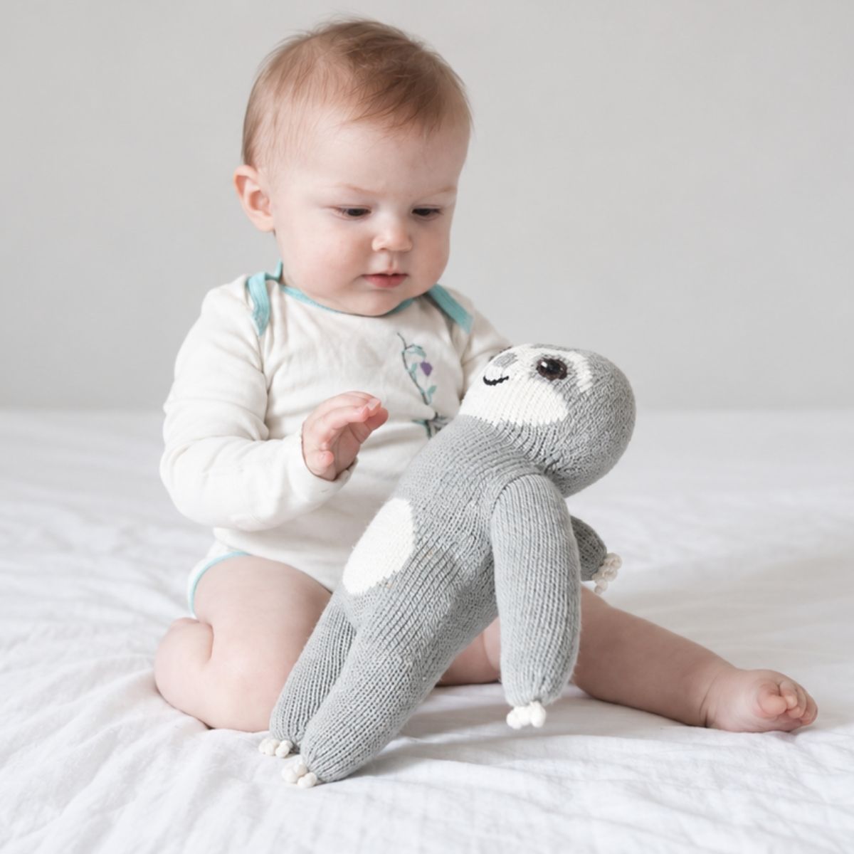 Baby spielt mit einem weichen Faultier Kuscheltier aus Bio-Baumwolle