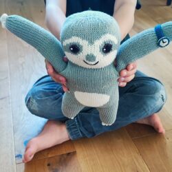 Kind hält ein handgestricktes Bio Kuscheltier Faultier mit blauer Armbanduhr in die Kamera