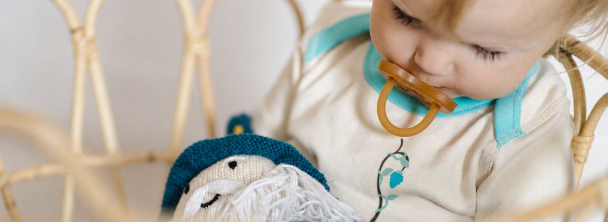 Kleinkind mit Schnuller kuschelt mit einer handgestrickten Bio-Puppe als Begleiter beim sanften Schnuller abgewöhnen.