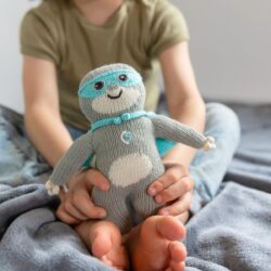 Kind hält das Kuscheltier Super Chilly zwischen den Füßen – Bio Faultier mit Maske und Cape