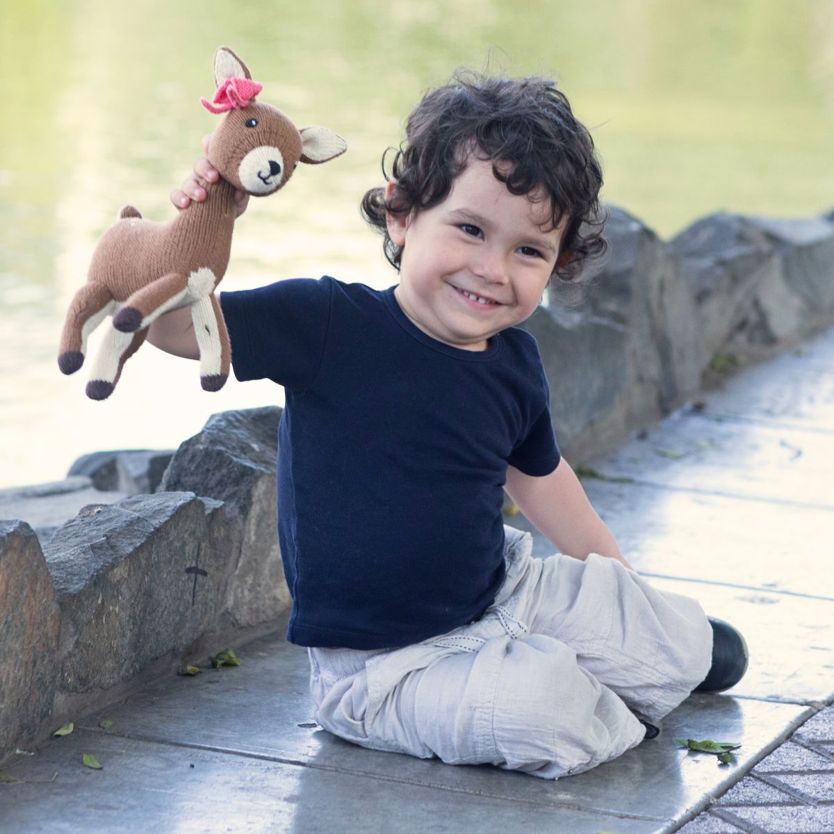 Junge hält ein Bio Kuscheltier Reh mit rosa Schleife am See in der Hand