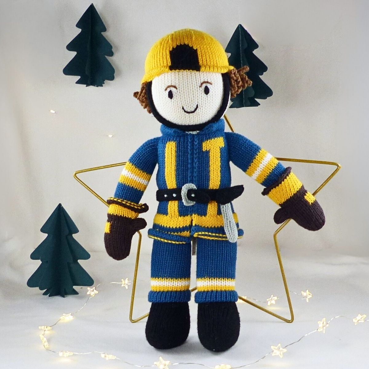 Handgestrickte Feuerwehrmann Puppe aus Bio-Baumwolle mit weihnachtlicher Deko, Lichterkette und kleinen Papierbäumen – nachhaltiges Kuscheltier von Chill n Feel.