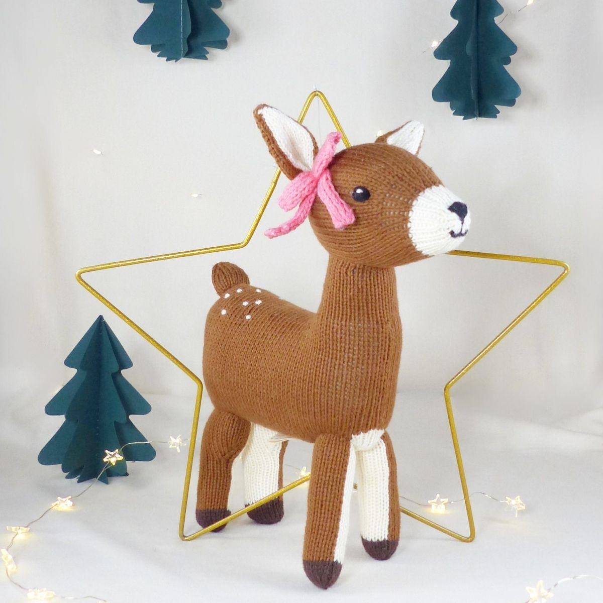 Handgestricktes Kuscheltier Reh aus Bio-Baumwolle mit rosa Schleife im weihnachtlichen Setting.
