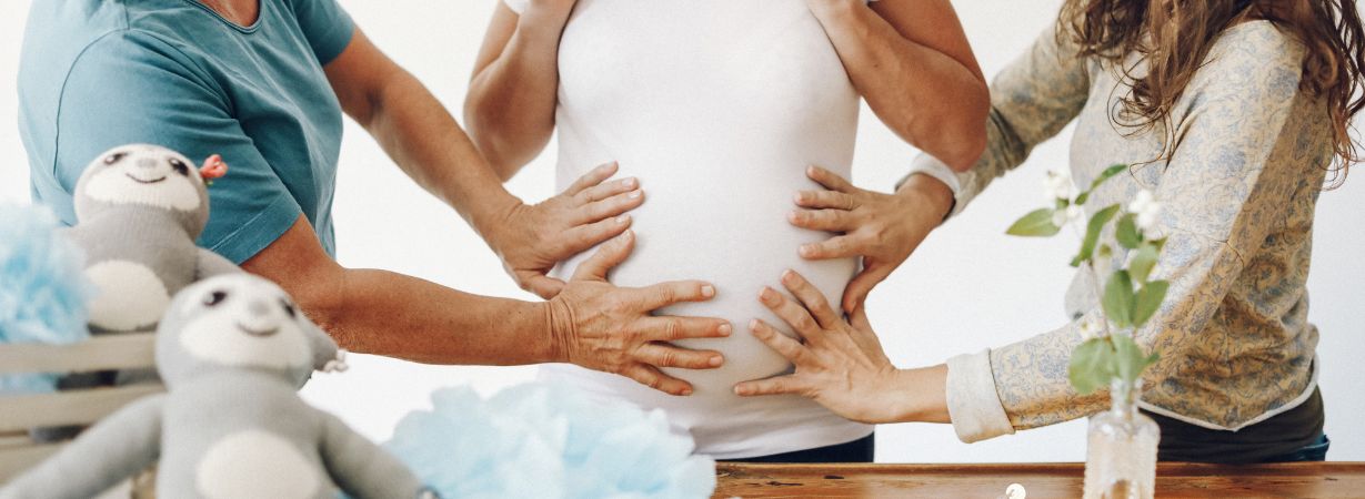 Hände am Babybauch bei einer Baby Shower Party mit gestrickten Faultieren, hellblauer Papierdeko und warmen Lichtern.