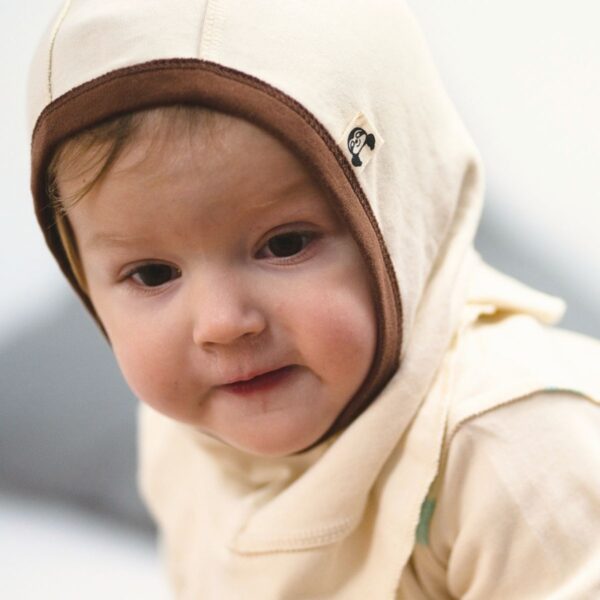 Baby mit beiger Schlupfmütze und braunem Rand aus Bio Pima Baumwolle, hautfreundlich und nahtlos, ideal bei Neurodermitis.