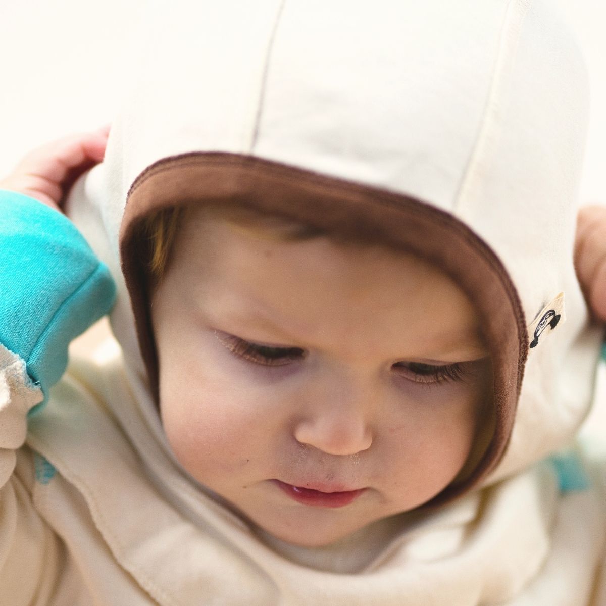 Baby mit Schlupfmütze aus Bio Baumwolle, zieht die Mütze zurecht, nahtlos und sanft für empfindliche Haut und Neurodermitis.
