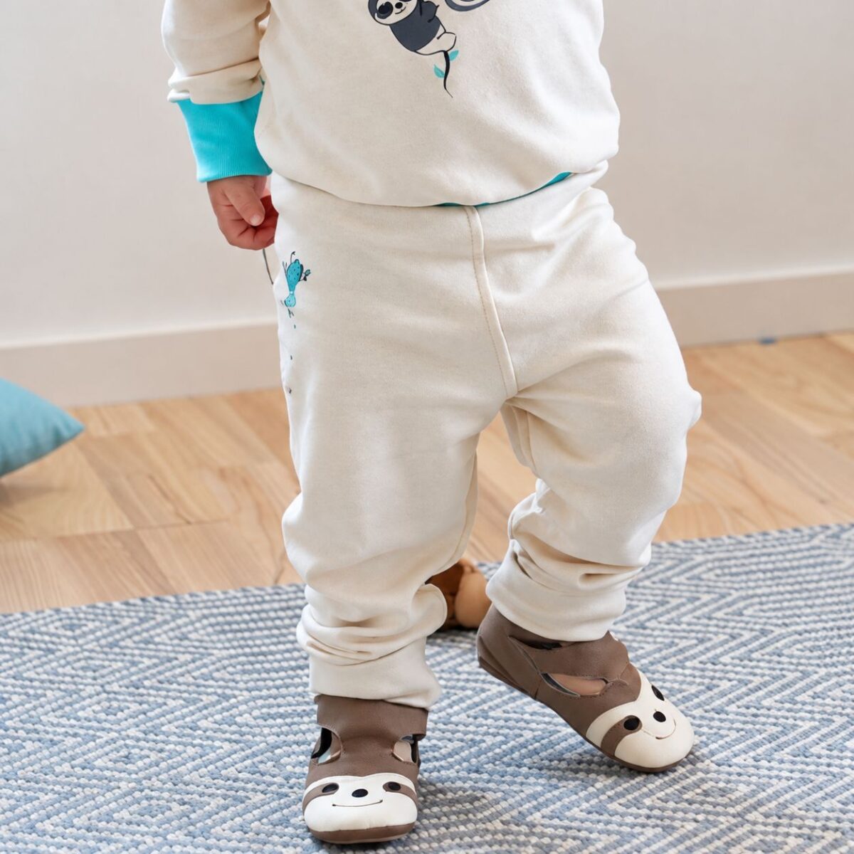 Kleinkind trägt cremefarbene Babyleggings bei Neurodermitis mit kleinem Faultiermotiv und weichen Beinbündchen.