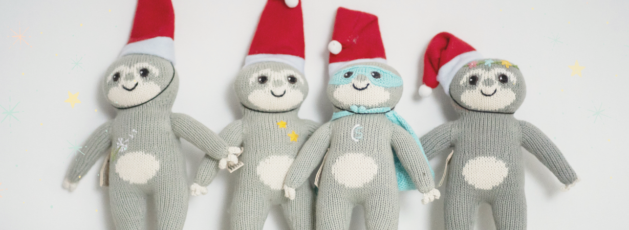 Vier handgestrickte Faultiere mit Weihnachtsmützen – ein liebevolles Ritual für Babys erstes Weihnachten: Wünsche sammeln im Weihnachtssäckchen.