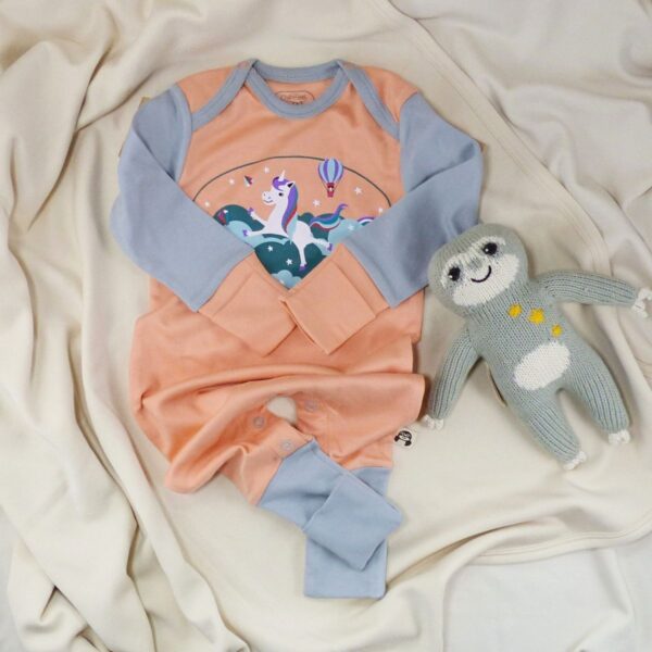Peachfarbener Babystrampler mit Einhornprint und grauem Faultier auf beigefarbener Decke