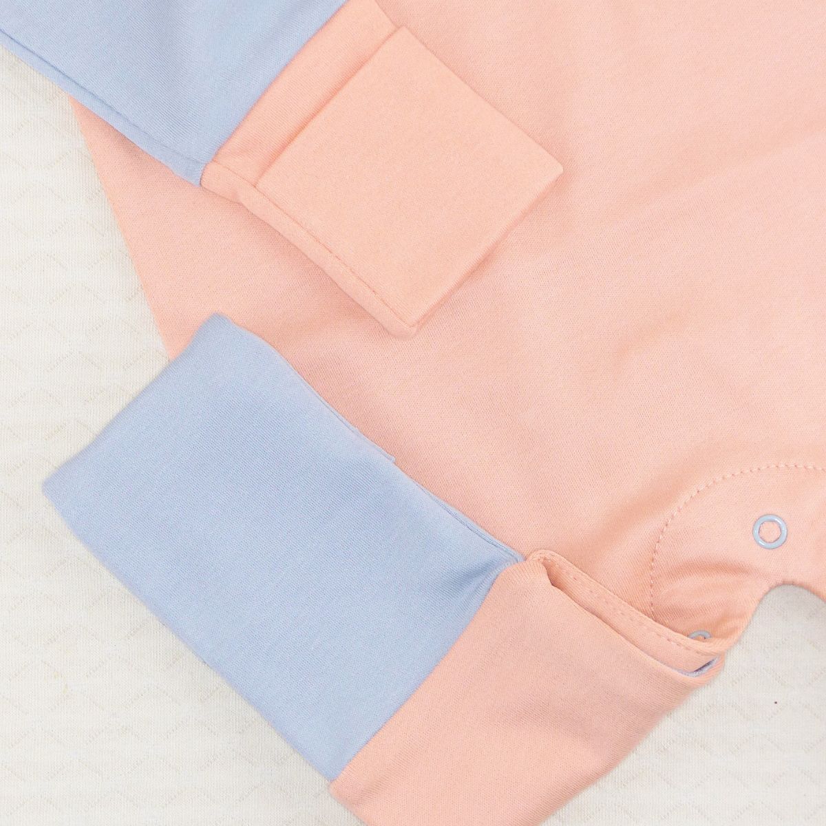 Close-up des Babystramplers mit umgeschlagenen Bündchen an Ärmeln und Beinen in Peach und Hellblau