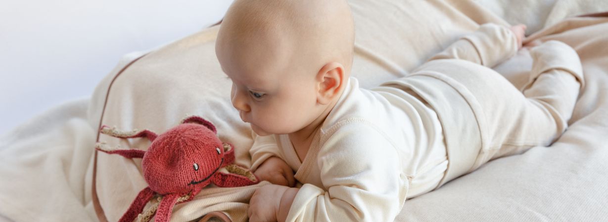 Baby spielt mit Kuscheltier-Oktopus, das an die Nabelschnur erinnert und Geborgenheit spendet – ideale Umgebung für hochsensible Babys.