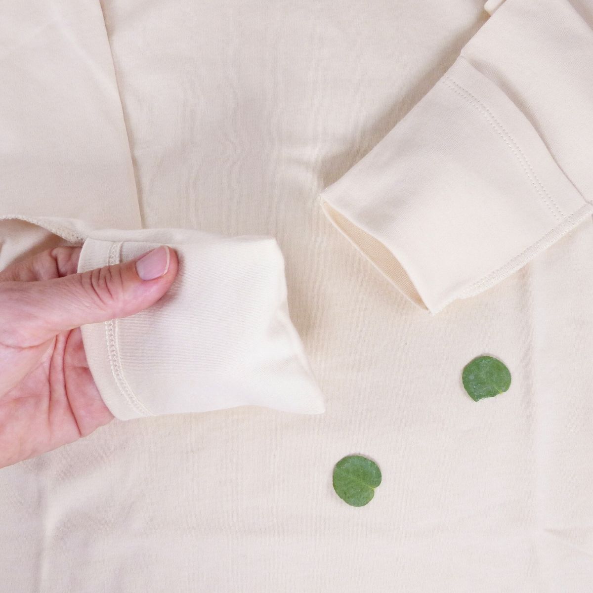Neurodermitis Langarmshirt – Detailansicht Kratzschutz Detailansicht Neurodermitis Langarmshirt in Natur – umklappbarer Kratzschutz am Ärmel wird mit der Hand demonstriert.