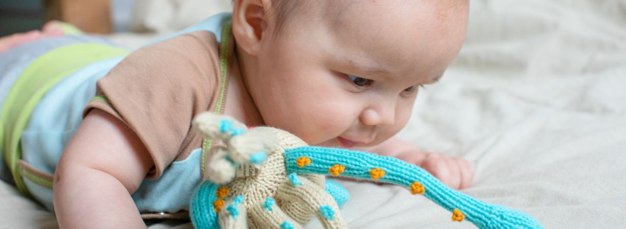 Ein Baby spielt mit den weichen Tentakeln eines Kuschel-Kalmars aus Bio-Baumwolle, die an die Nabelschnur erinnern und Geborgenheit spenden.