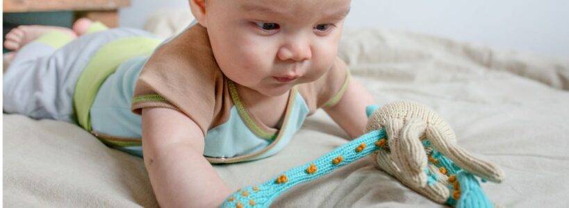 Baby spielt neugierig mit bio Kuscheltieren aus Baumwolle auf dem Bett