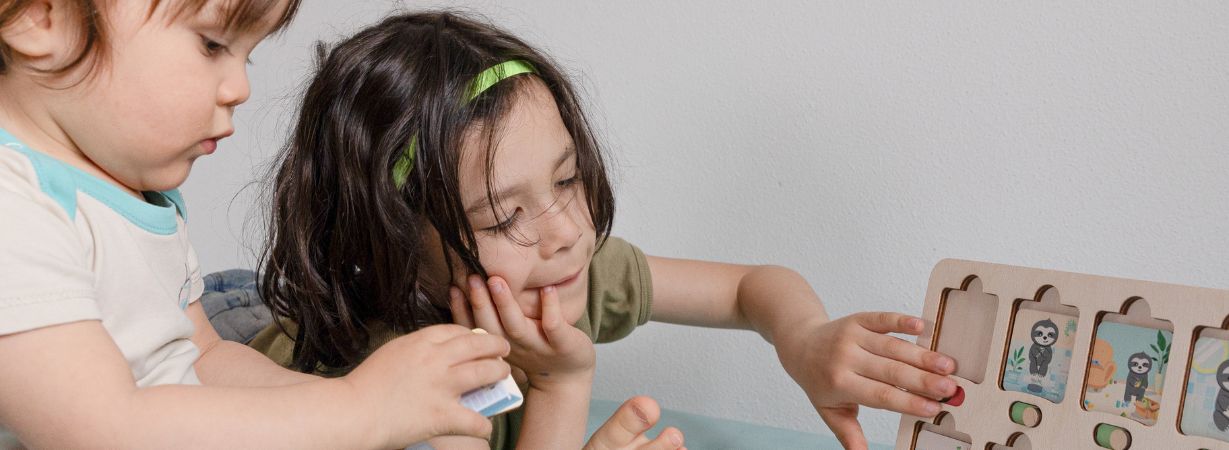 Großer Bruder benutzt den Lernrahmen der Faultier-Abendroutine, während der kleine Bruder mit einer Routinekarte daneben sitzt