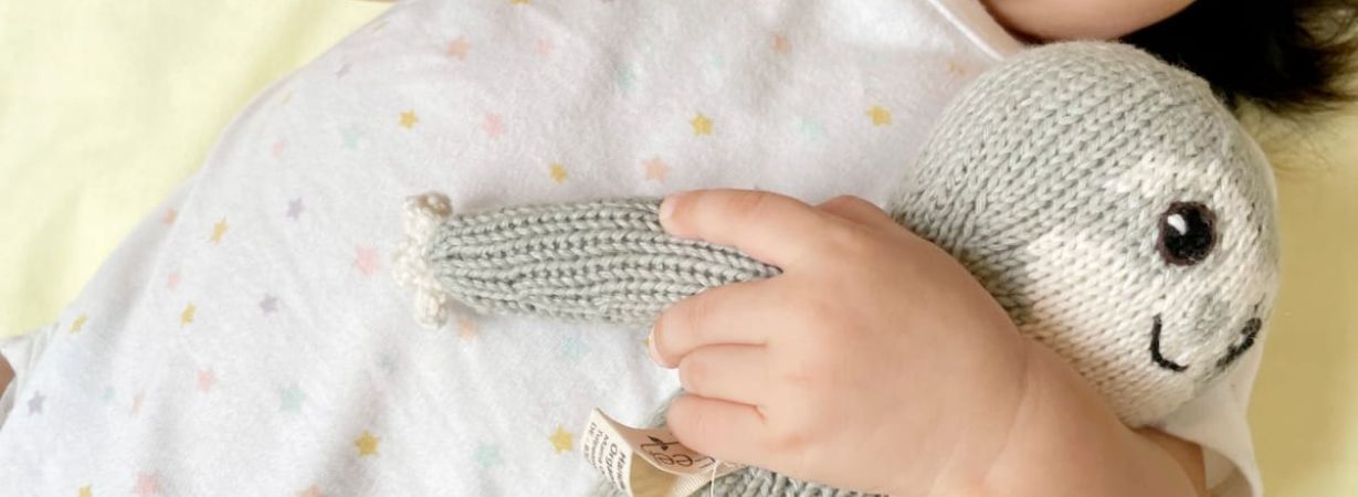 Kleine Kinderhand umarmt Kuscheltier Faultier Chilly, das Teil der Abend Routine ist