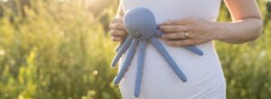 Schwangere Frau hält ein Tentakel Kuscheltier vor ihren Babybauch – inspiriert von der Nabelschnur und beliebt bei Frühchen und Neugeborenen