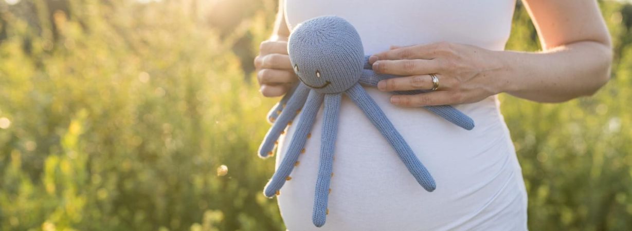 Schwangere Frau hält ein Tentakel Kuscheltier vor ihren Babybauch – inspiriert von der Nabelschnur und beliebt bei Frühchen und Neugeborenen