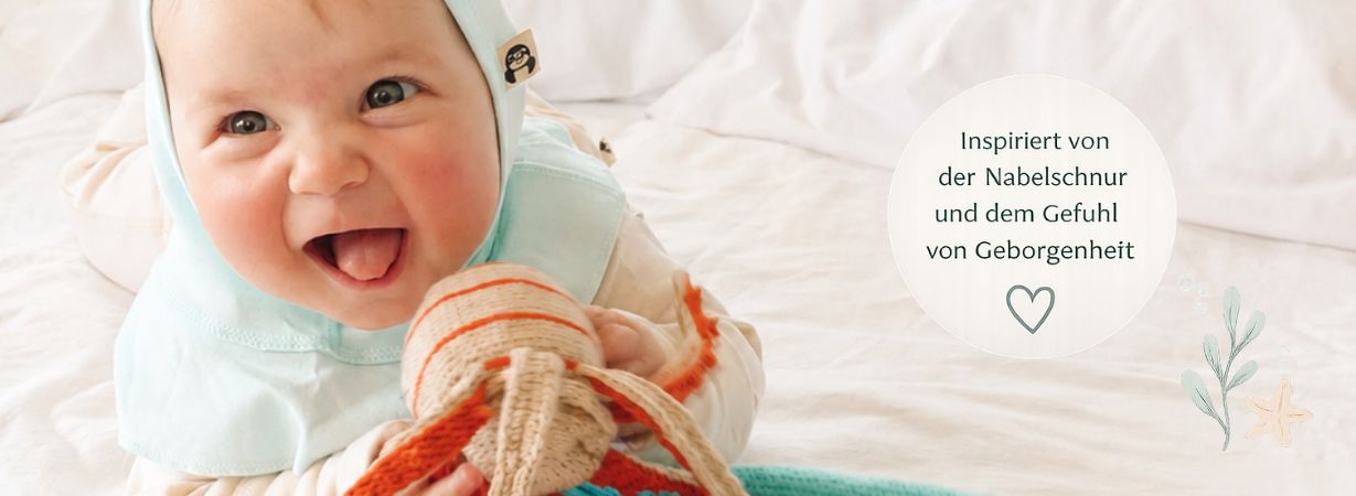 Lachendes Baby kuschelt mit einem Tentakel Kuscheltier inspiriert von der Nabelschnur und dem Gefühl von Geborgenheit