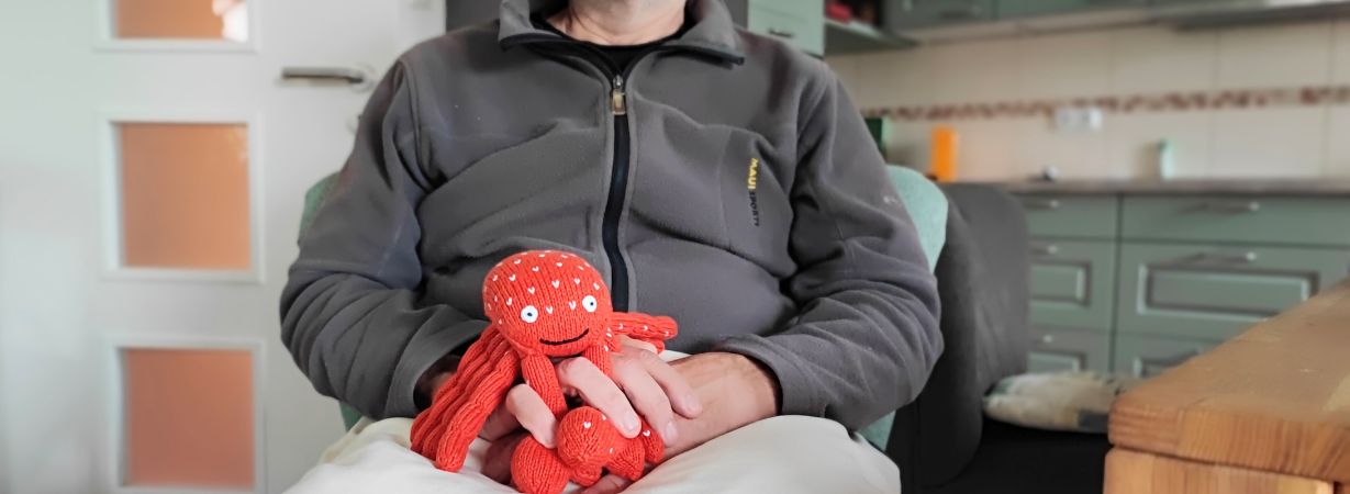 Hände eines dementen Mannes mit einem Kuscheltierkrebs zwischen den Fingern zur Kontrakturprophylaxe bei Demenz