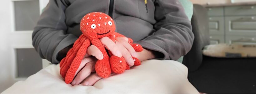 Hände eines dementen Mannes mit einem Kuscheltierkrebs zur Kontrakturprophylaxe bei Demenz