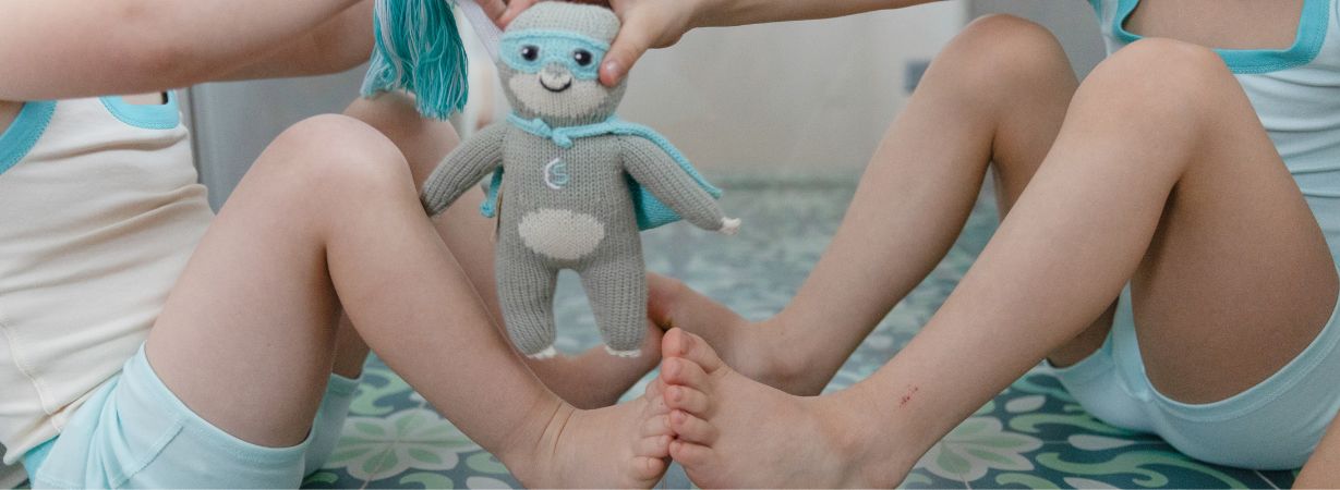 Füße zweier Kinder berühren sich mit Kuscheltier Faultier Chilly in der Mitte – ideal für autistische Kinder mit Berührungsempfindlichkeit.