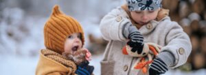 Zwei Kinder spielen im Schnee, warm eingepackt in Kleidung aus Pima Baumwolle, ideal für empfindliche Haut bei Winterekzem.
