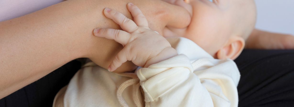 Mama hält ihr Baby beim Känguruhen auf der Brust. Das Baby trägt weiche Kleidung aus Pima-Baumwolle, die den Hautkontakt perfekt ergänzt.