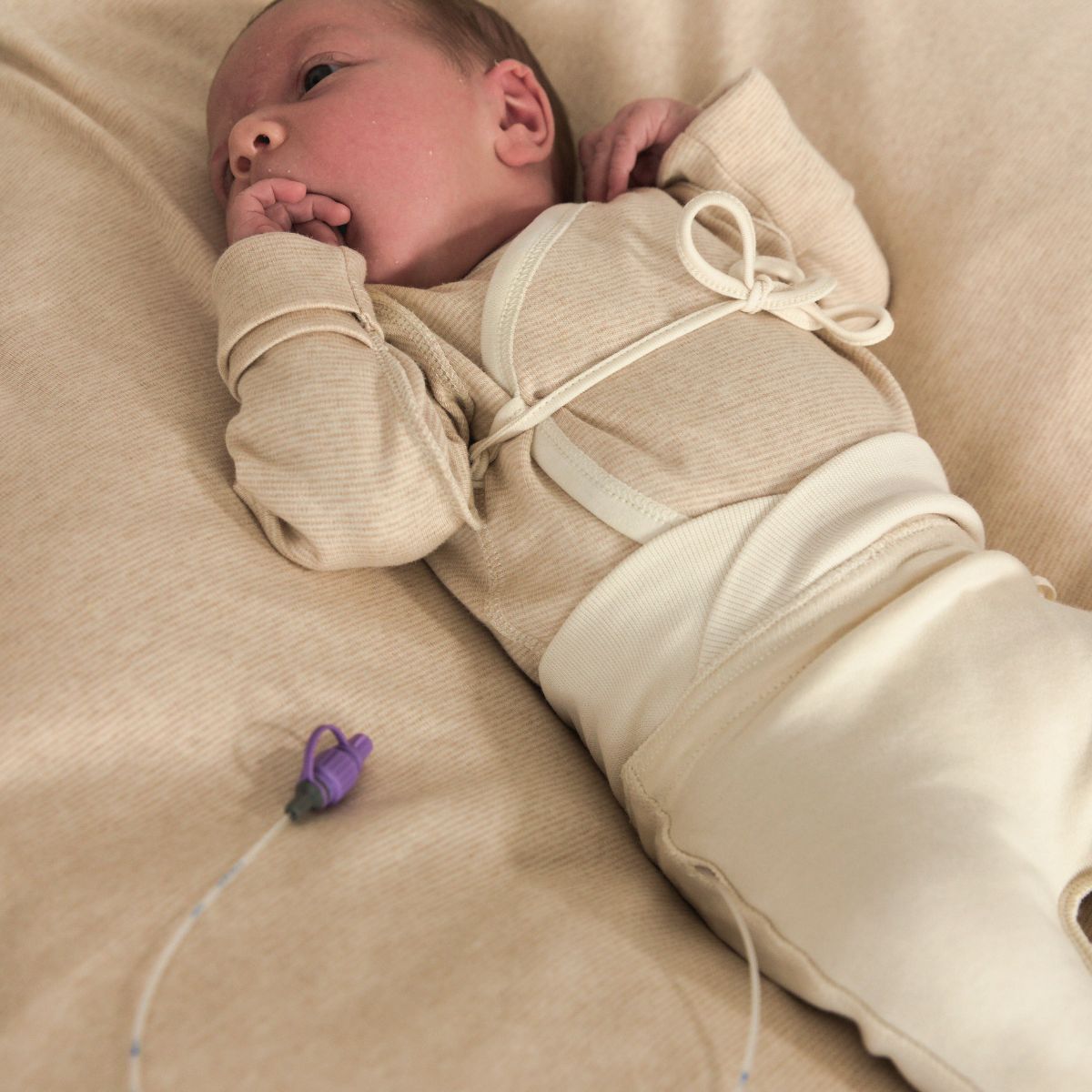 Frühchen trägt Hose mit Nabelbund und seitlichem Schlauchauslass aus Bio Pima Baumwolle auf weicher Unterlage