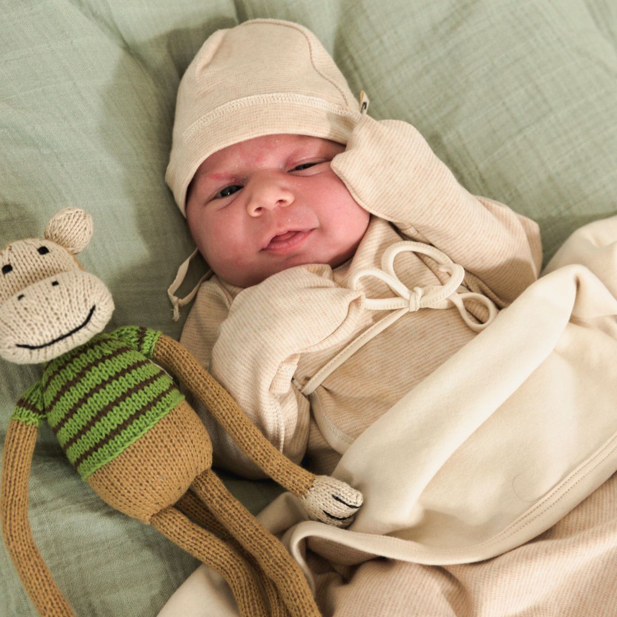 Frühchen mit weicher Bio Mütze aus Pima Baumwolle und Kuscheltier auf hellgrüner Decke