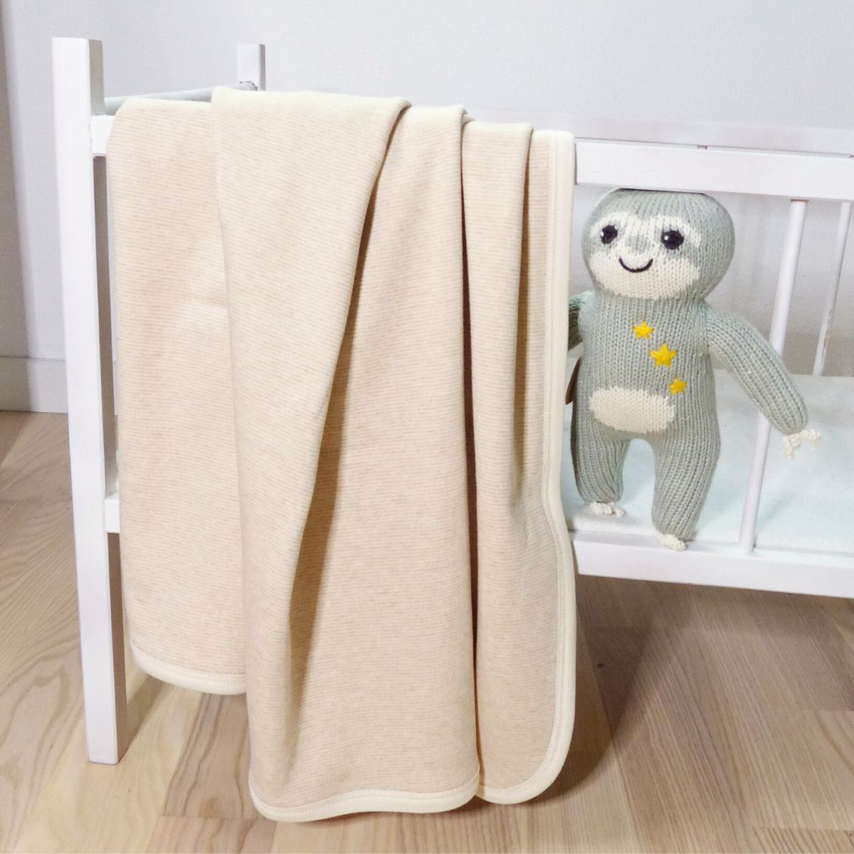Bio Babydecke aus Pima Baumwolle in Beige, weich drapiert über einem Kinderbett mit gestricktem Faultier von Chill n Feel