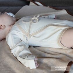 Baby liegt entspannt auf einer zweilagigen Bio-Baumwolldecke aus Pima Baumwolle mit brauner Einfassung