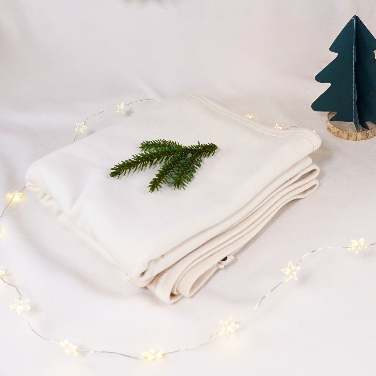 Bio Babydecke aus Pima Baumwolle, weich und handgefertigt, liebevoll drapiert mit Tannenzweig und Lichterkette.