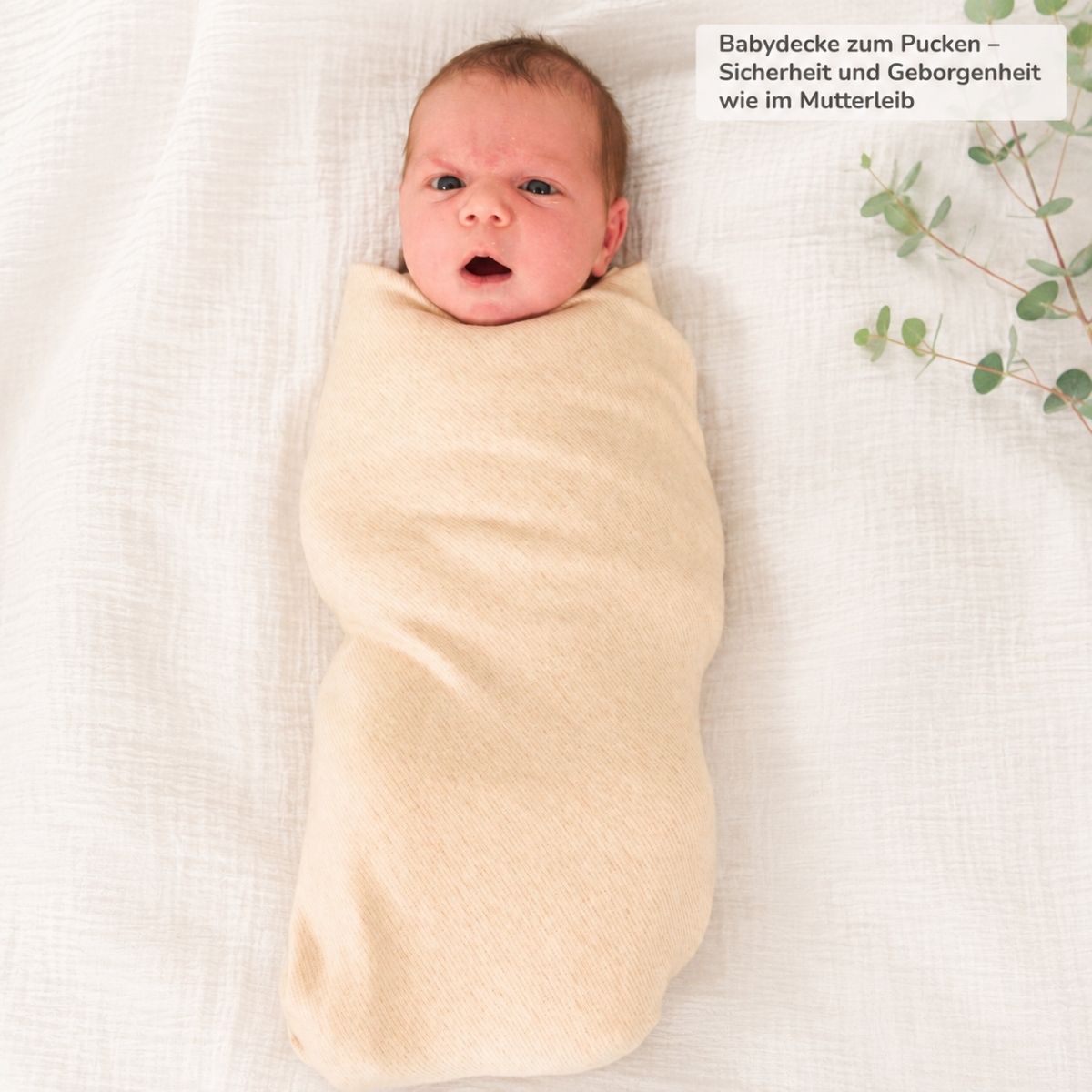 Neugeborenes Baby mit Bio Babydecke aus Pima Baumwolle gepuckt auf hellem Stoffhintergrund