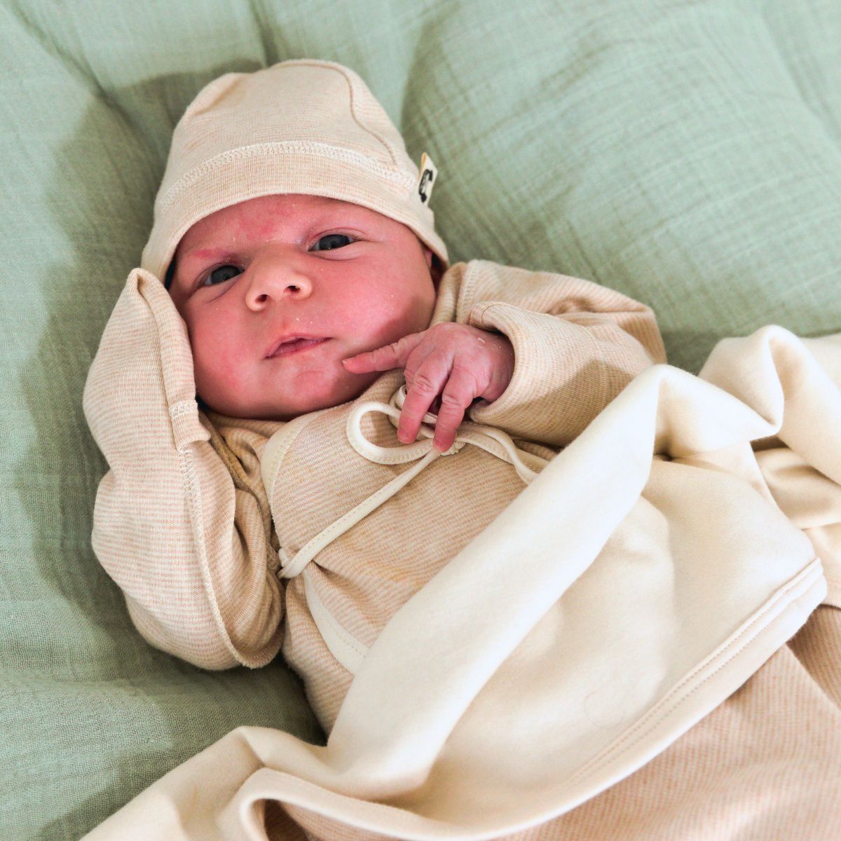 Frühchen Body aus Bio-Pima-Baumwolle mit Wickelverschluss und Umschlagbündchen, getragen von einem Baby auf weichem grünem Untergrund