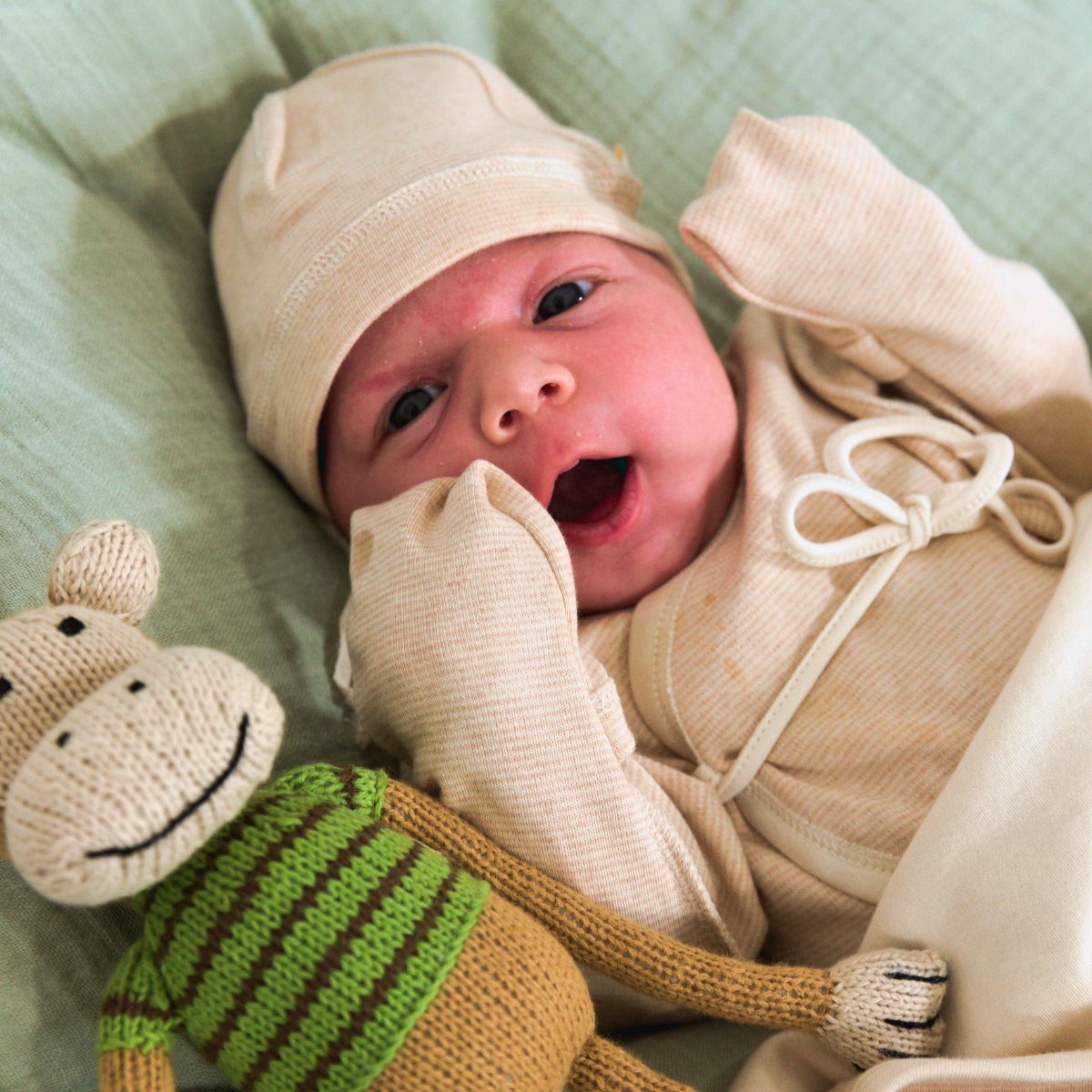 Frühchen trägt einen Wickelbody aus Bio-Pima-Baumwolle mit Umschlagbündchen und Mütze, neben ihm liegt ein handgestricktes Kuscheltier von Chill n Feel