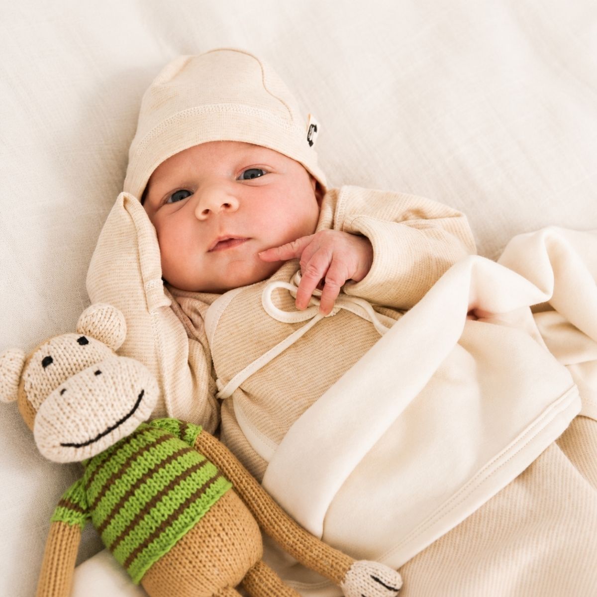 Neugeborenes Baby in weichem Frühchen Body aus Bio Pima Baumwolle mit Umschlagbündchen und Mütze in naturbeige