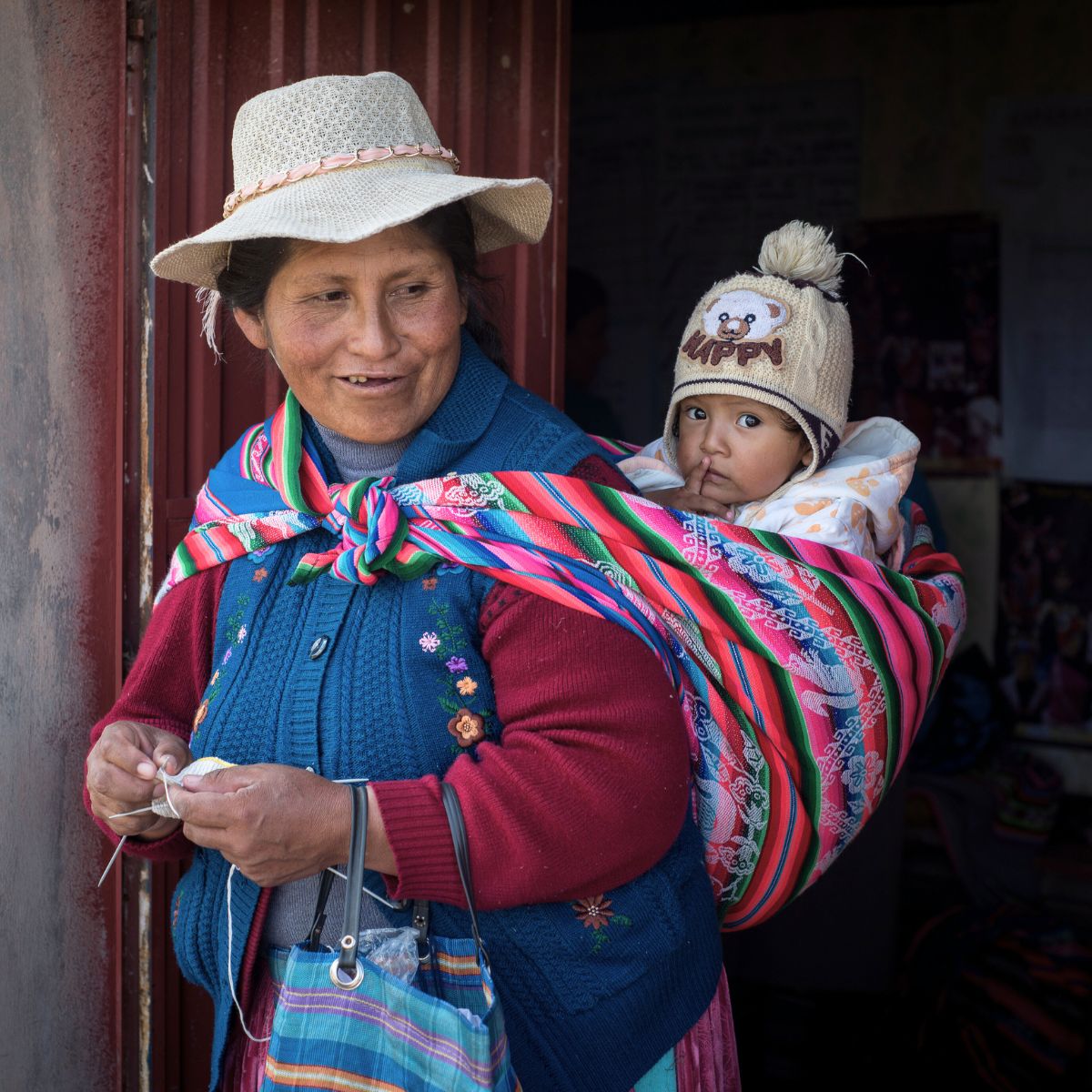 Frau in Peru strickt mit Baby auf dem Rücken – Ursprung der gestrickten Kuscheltiere