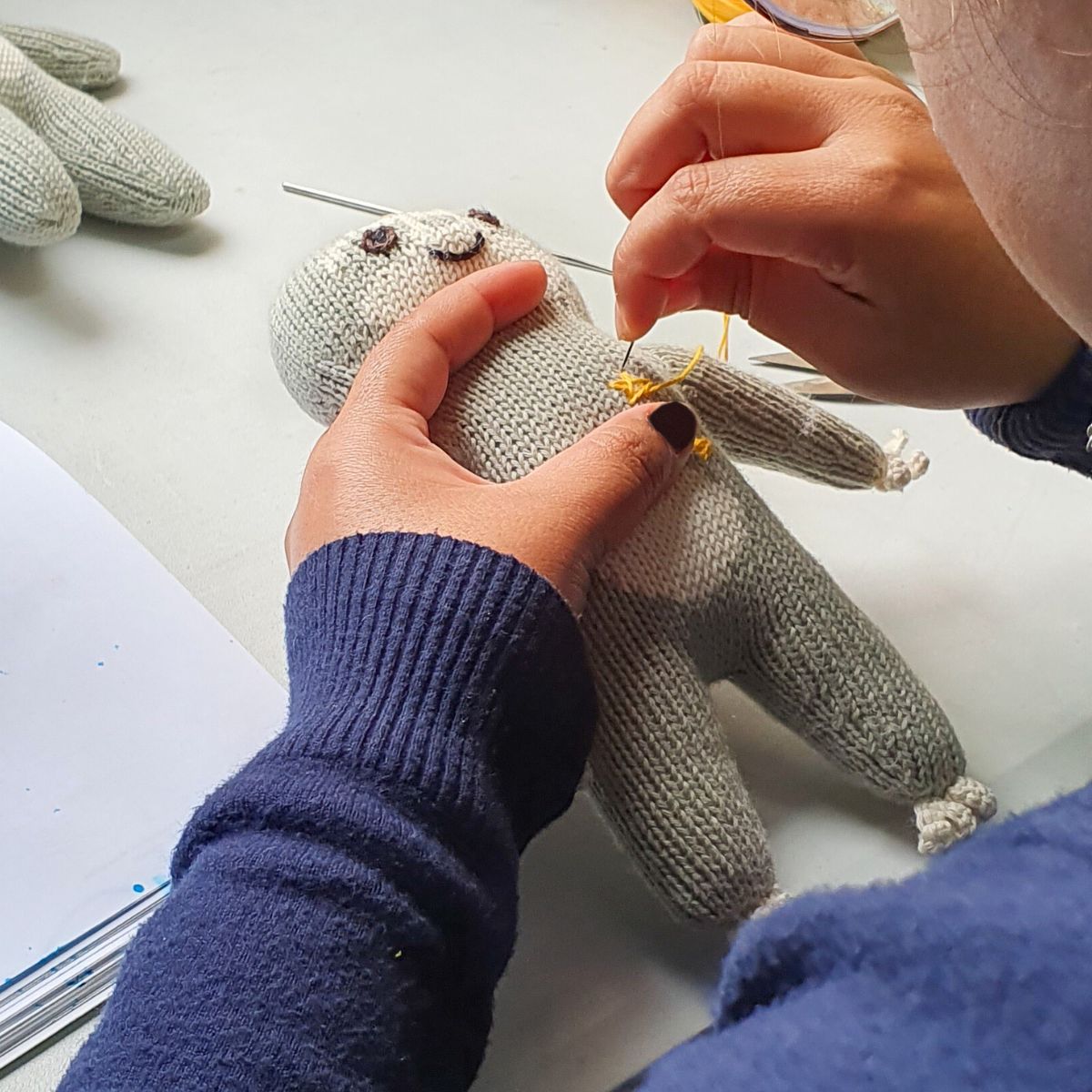 Frau stickt per Hand an einem gestrickten Kuscheltier in Faultierform – liebevolle Handarbeit in Peru