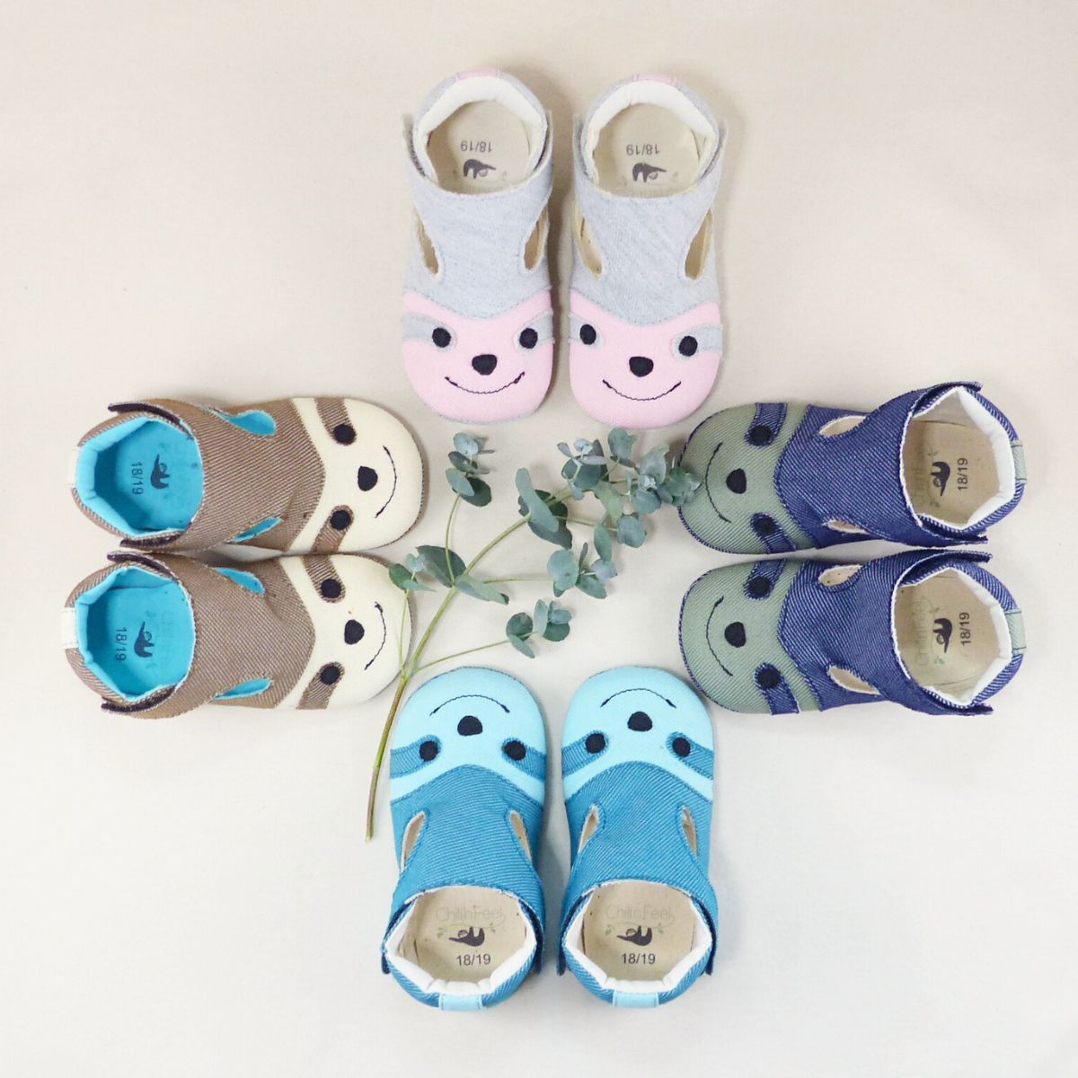 Vegane Babyschuhe „Meine ersten Schritte“ in fünf Farbvarianten, kreisförmig angeordnet mit Eukalyptus