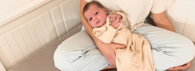 Ein Neugeborenes liegt entspannt im Arm eines Elternteils und trägt einen weichen Bio-Strampelsack aus Pima-Baumwolle. Die Kleidung von Chill n Feel schenkt Frühchen und Neugeborenen Geborgenheit, Wärme und Ruhe – wie im Mutterleib.