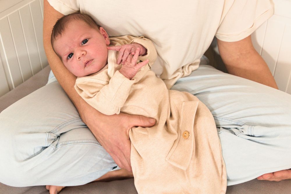 Neugeborenes liegt entspannt im Arm eines Elternteils und trägt einen weichen Strampelsack aus Bio-Baumwolle. Die Kleidung von Chill n Feel schenkt Frühchen und Neugeborenen Geborgenheit, Wärme und Bewegungsfreiheit.