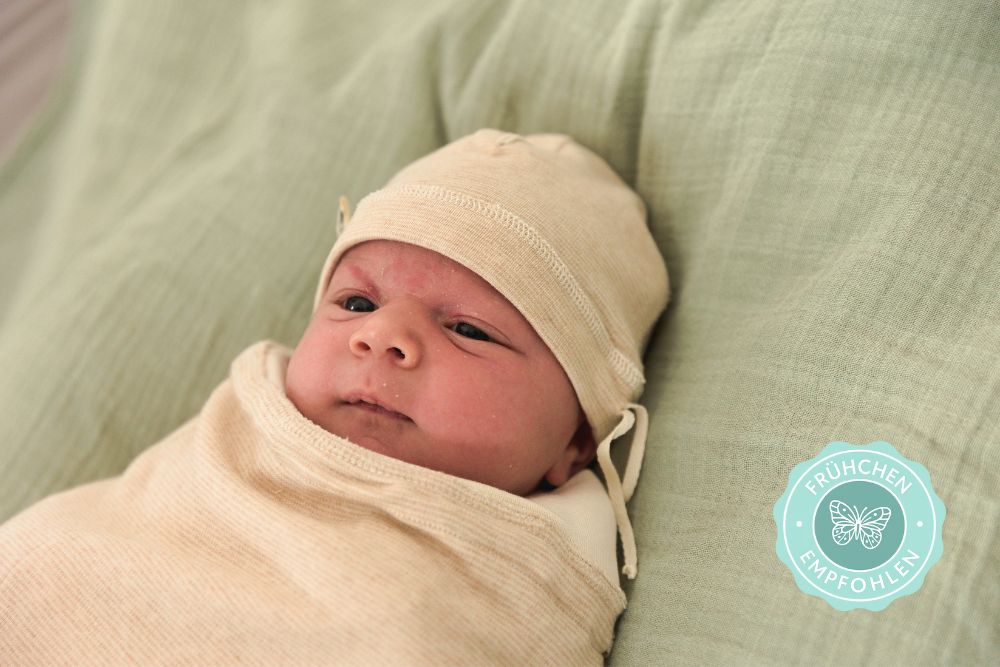 Baby in weicher Bio-Baumwoll-Decke eingewickelt. Das Neugeborene trägt eine Mütze und liegt entspannt, sicher eingepuckt auf einem mintgrünen Tuch. Ideal zum Pucken für Frühchen und Neugeborene, empfohlen von Chill n Feel.