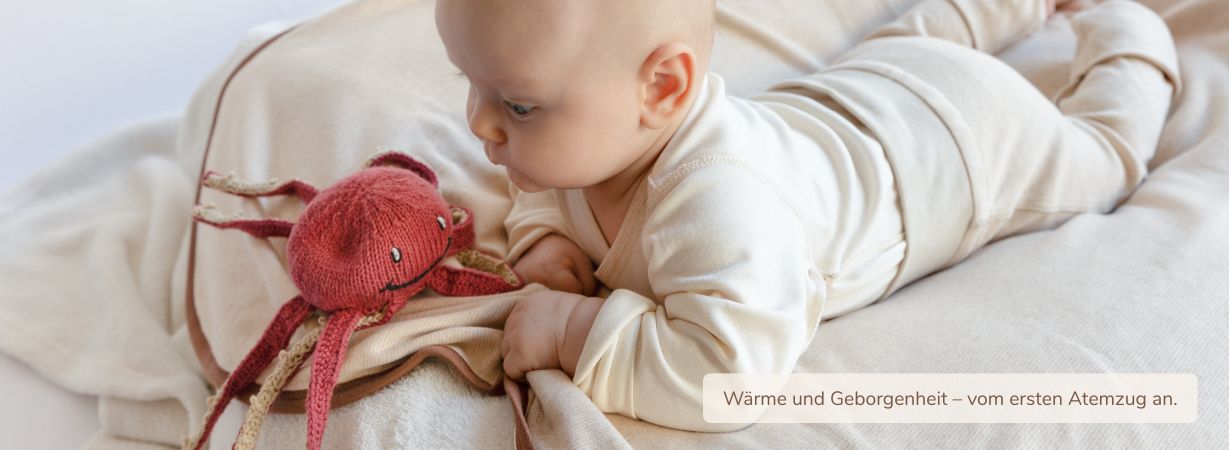 Baby liegt auf weicher Bio-Babydecke aus Pima Baumwolle und greift nach seinem Kuscheltier – sanfte Geborgenheit und Wärme von Anfang an.