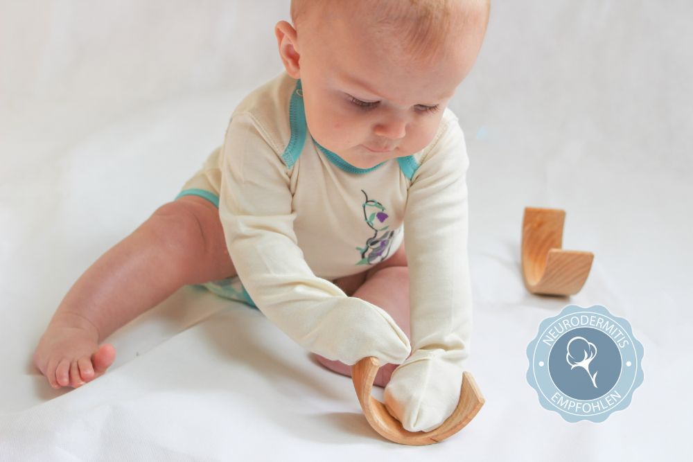 Baby mit Neurodermitis trägt hautfreundliche Kleidung aus Pima Bio-Baumwolle mit Kratzschutz an den Händen