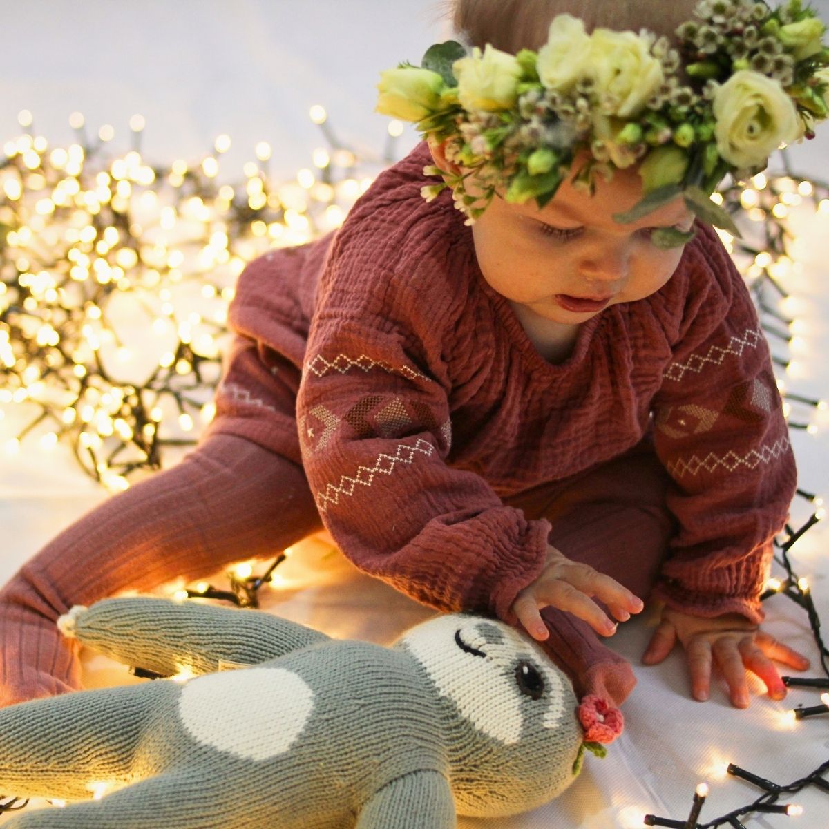Baby spielt mit nachhaltigem Kuscheltier zwischen warmen Weihnachtslichtern – ein liebevolles, nachhaltiges Weihnachtsgeschenk aus Bio-Baumwolle.