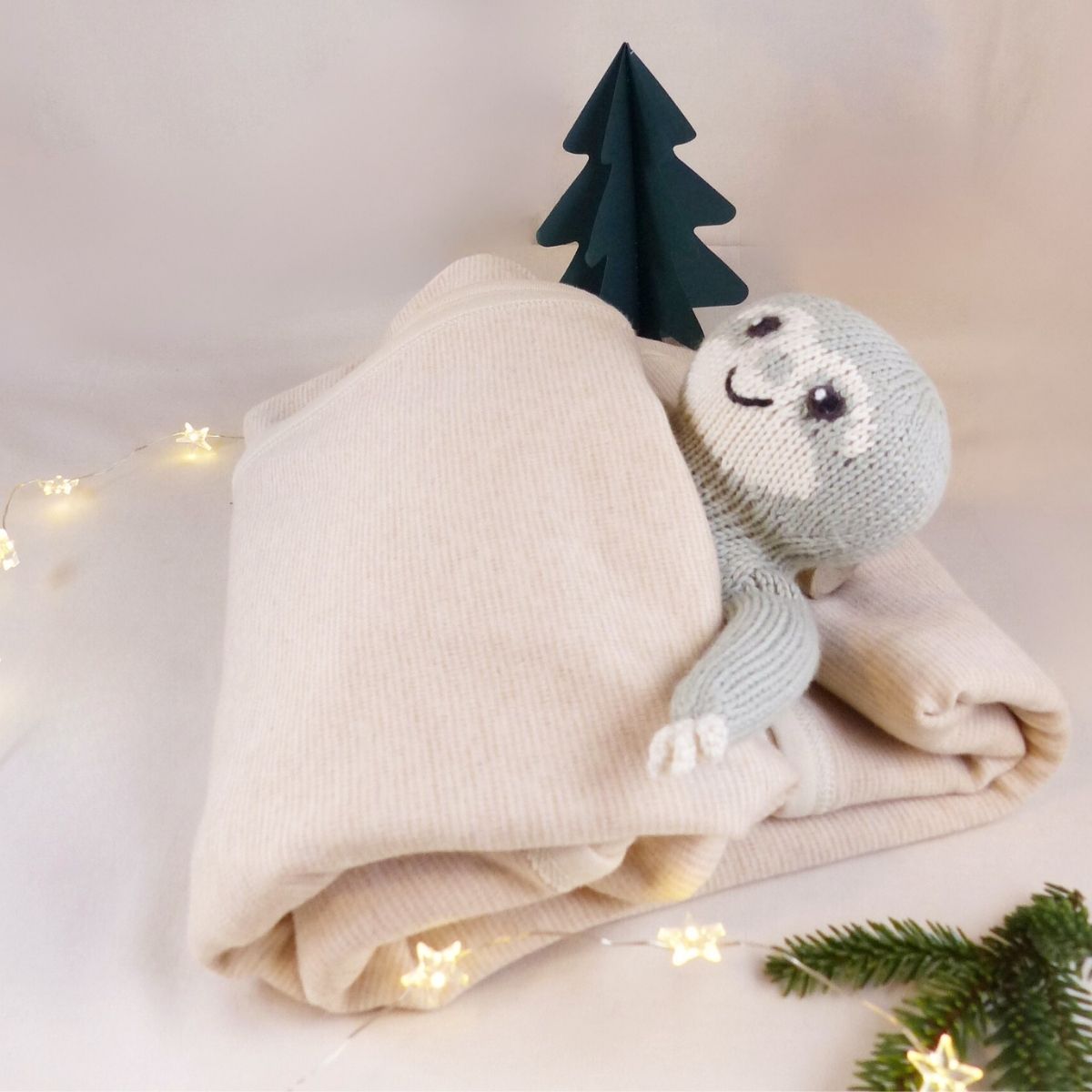 Bio Babydecke aus Pima Baumwolle als nachhaltiges Weihnachtsgeschenk, liebevoll inszeniert mit Lichterkette, kleinem Tannenbaum und Faultier-Kuscheltier.